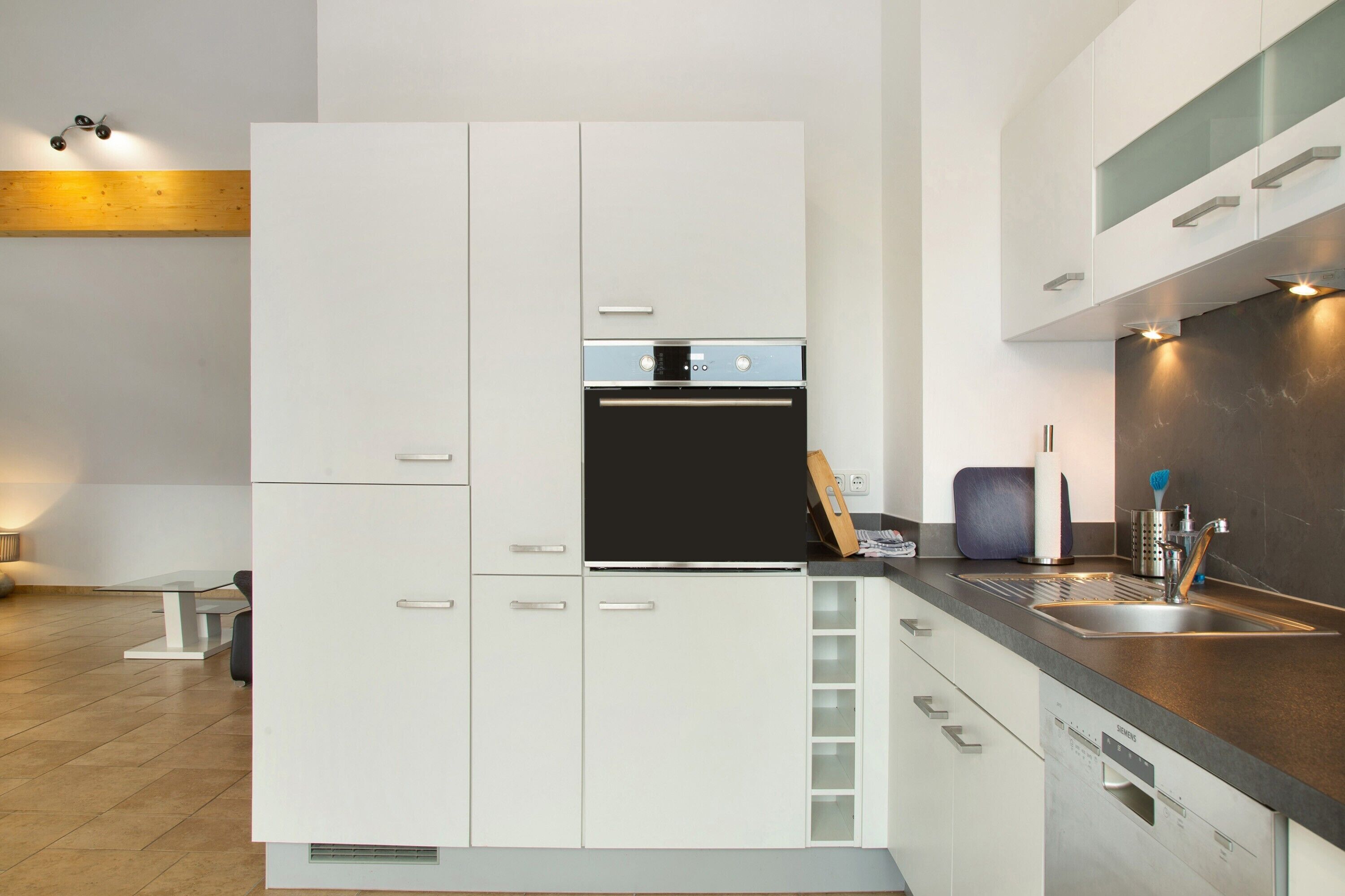 Una cocina moderna con armarios blancos, horno empotrado y pileta de acero inoxidable.