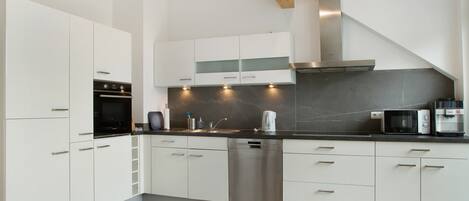 A modern kitchen with white cabinets, a stainless steel dishwasher, a microwave, and a coffee maker.