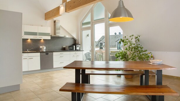 Une cuisine moderne avec des meubles blancs, une table en bois et un luminaire suspendu.