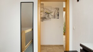Un couloir avec un escalier en bois, un miroir et une œuvre d’art accrochée au mur.