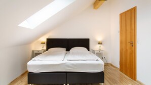 Une chambre à coucher avec un lit, des tables de chevet, une porte en bois et un puits de lumière.