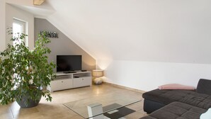 Un salon moderne avec un téléviseur à écran plat, une plante en pot, un canapé et une lampe.