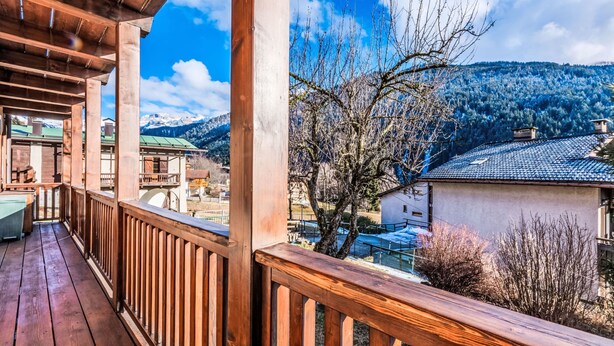 A wooden balcony with a view of a mountainous landscape and a building with a tiled roof.