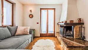 A cozy living room with a grey sofa, a white fur rug, a fireplace with copper pots, and a wooden floor.