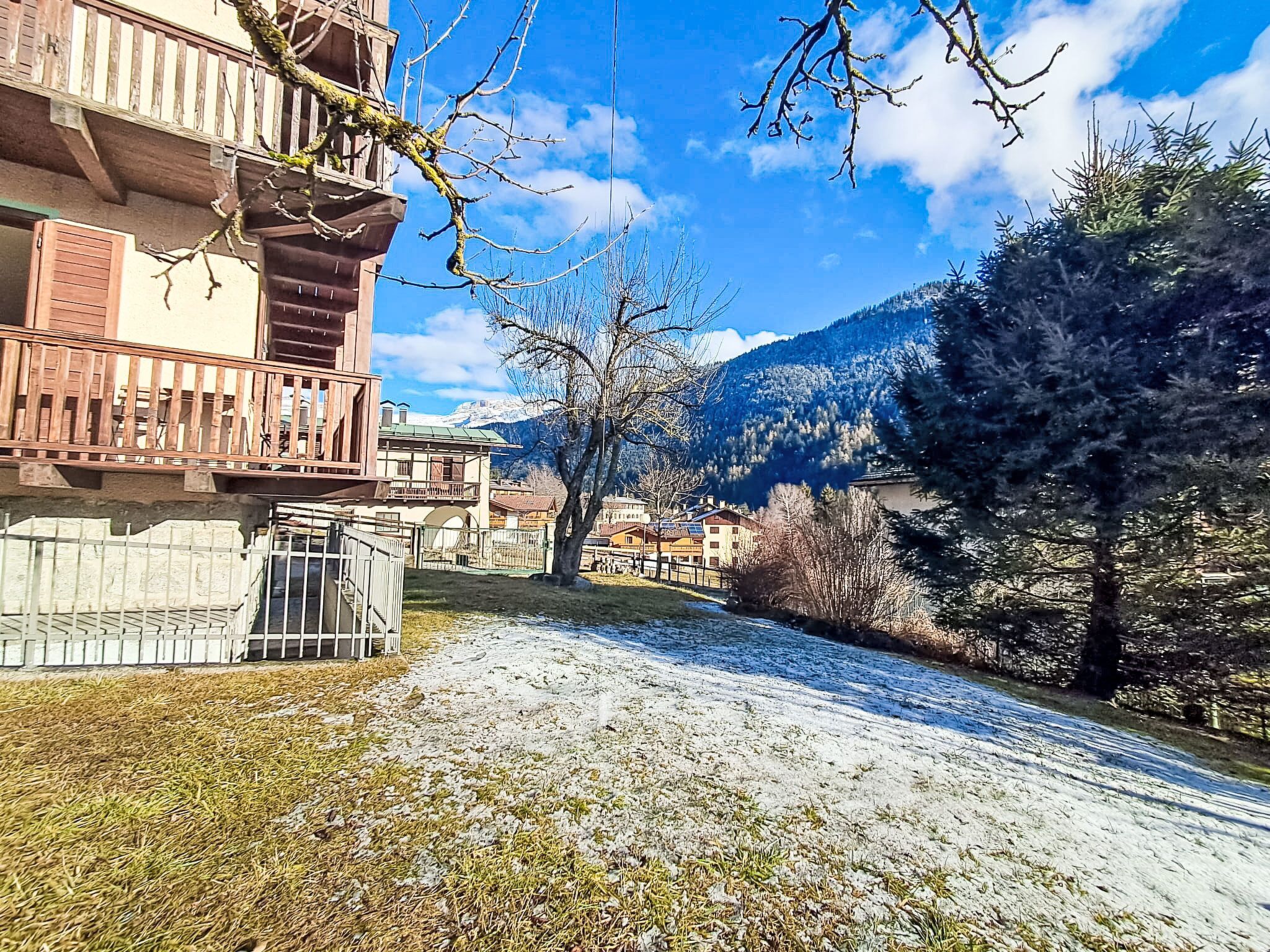 Un bâtiment doté d’un balcon, un sentier enneigé et un paysage montagneux en arrière-plan.