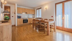 A modern kitchen with wooden cabinets, a dining area with a table and chairs, and a large sliding glass door leading to a balcony.