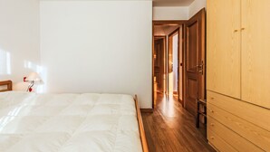 A bedroom with a bed, a wooden wardrobe, and a hallway leading to another room.