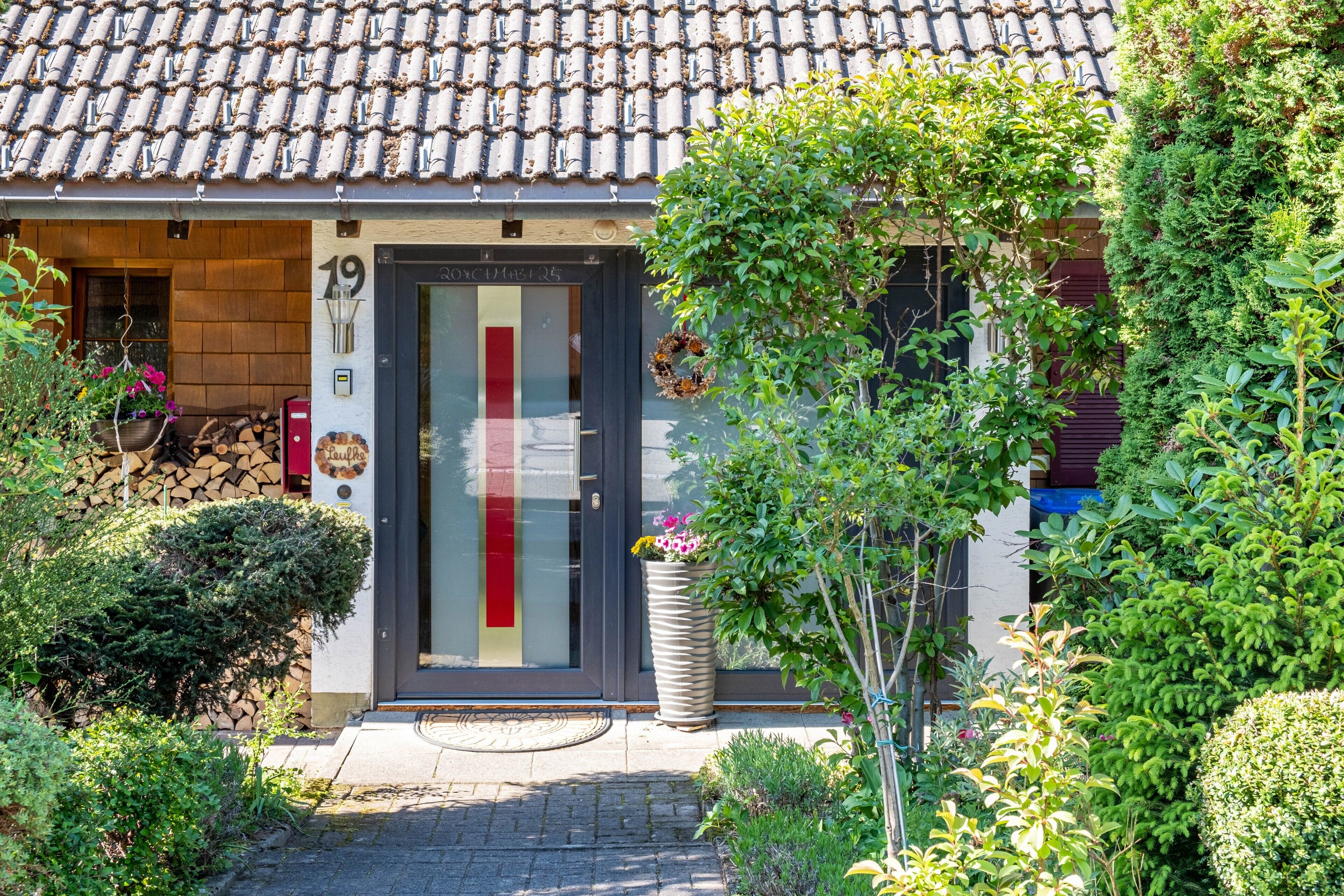 Een gebouw met een pannendak, een deur met een nummer en een bloempot ervoor.