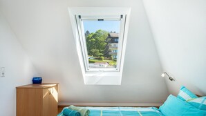 Ett sovrum med ett takfönster, en säng med blått sänglinne, ett träskåp och ett litet bord med en blå skål.