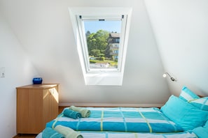 A bedroom with a skylight, a bed with blue bedding, a wooden cabinet, and a small table with a blue bowl.