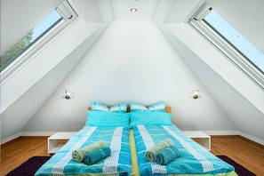Une chambre avec un puits de lumière, un lit avec une literie bleue et un plancher en bois.