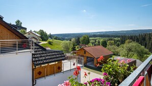 En bostadsbyggnad med en balkong, en liten träkonstruktion och utsikt över en grön dal.