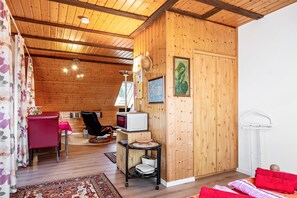 Habitación con paneles de madera, un comedor, una silla roja, un microondas, una mesita y una cama con almohadas rojas.