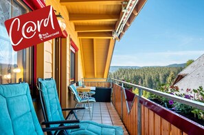 A balcony with chairs and a table, a wooden ceiling, and a view of a forested area. - Apartment 'Feldberg' with Mountain View, Southwest Balcony, Table Tennis, and Wi-Fi (Lenzkirch)