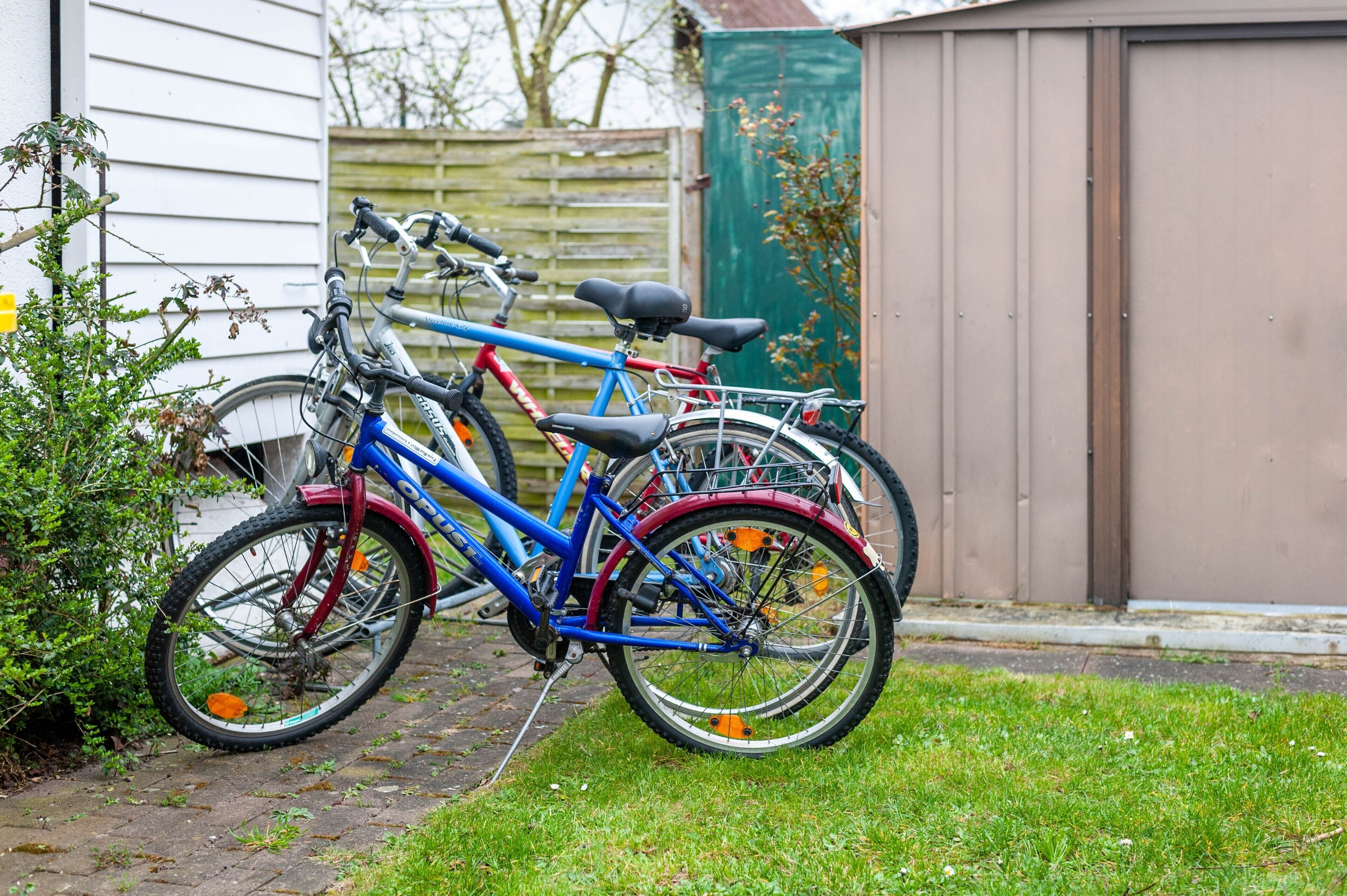En cykel parkeret ved et hus med et træhegn og et skur i baggrunden.