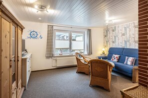 Une pièce avec un canapé bleu, des fauteuils en osier, un meuble en bois et une fenêtre avec des rideaux.