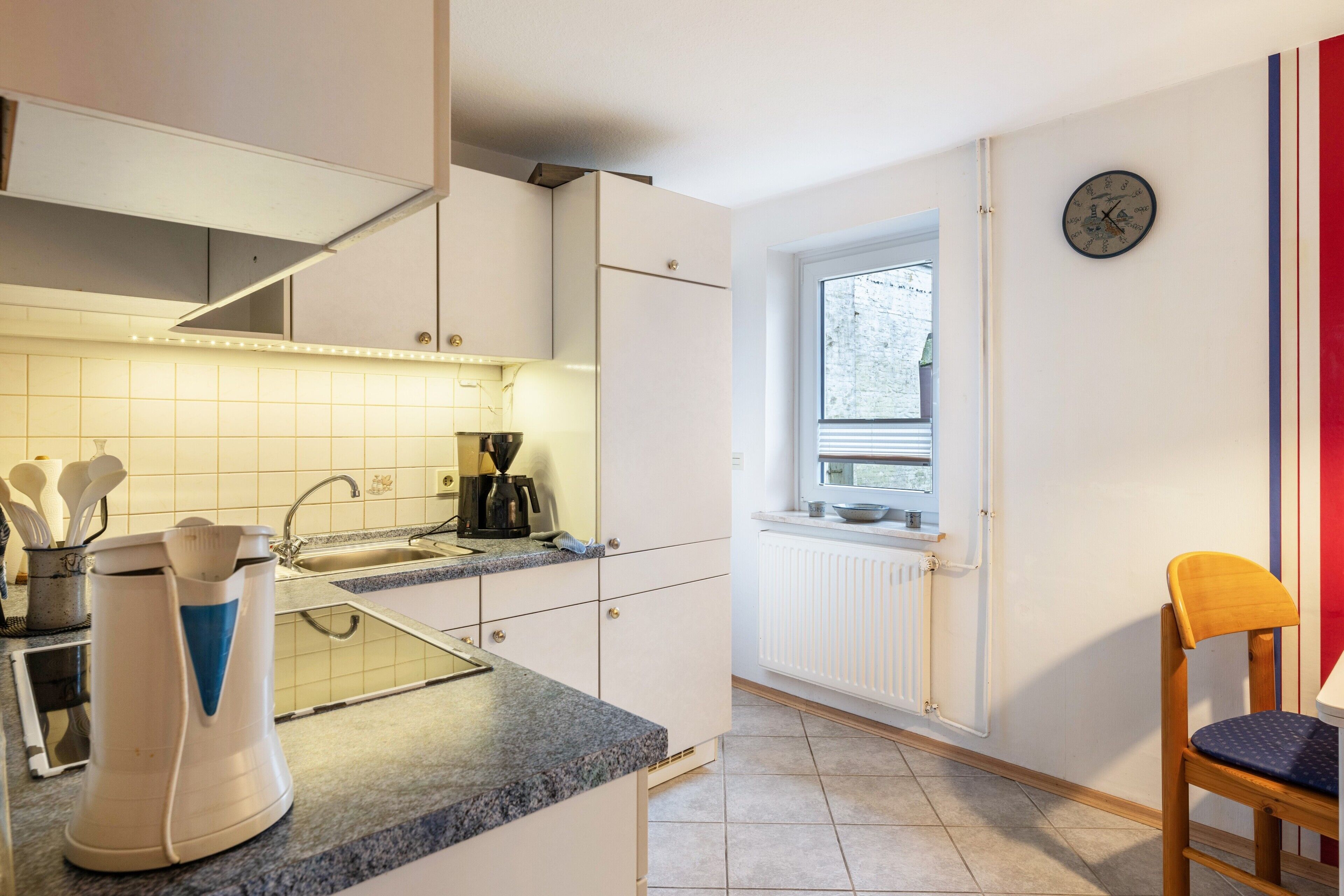 Une cuisine avec une fenêtre, une horloge et une chaise.