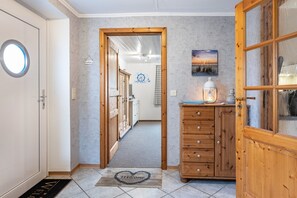 Un couloir avec une porte en bois, un paillasson, une armoire et un tableau accroché au mur.