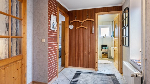 En hall med träpanel på väggarna, ett element och en klädstång som hänger på väggen.