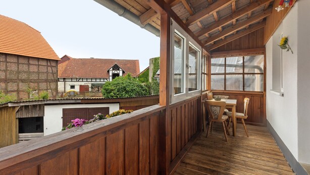 A wooden balcony with a table and chairs, a view of traditional houses, and a greenhouse. - Apartment 'Sonnenblume' with Balcony and Wi-Fi (Lichtenfels)