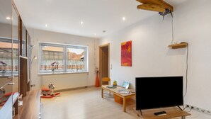 A modern living room with a flat-screen TV, wooden furniture, a window with curtains, and a ceiling fan. - Apartment 'Sonnenblume' with Balcony and Wi-Fi (Lichtenfels)