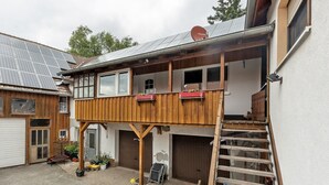 A two-story building with a wooden balcony, solar panels, and a garage. - Apartment 'Sonnenblume' with Balcony and Wi-Fi (Lichtenfels)