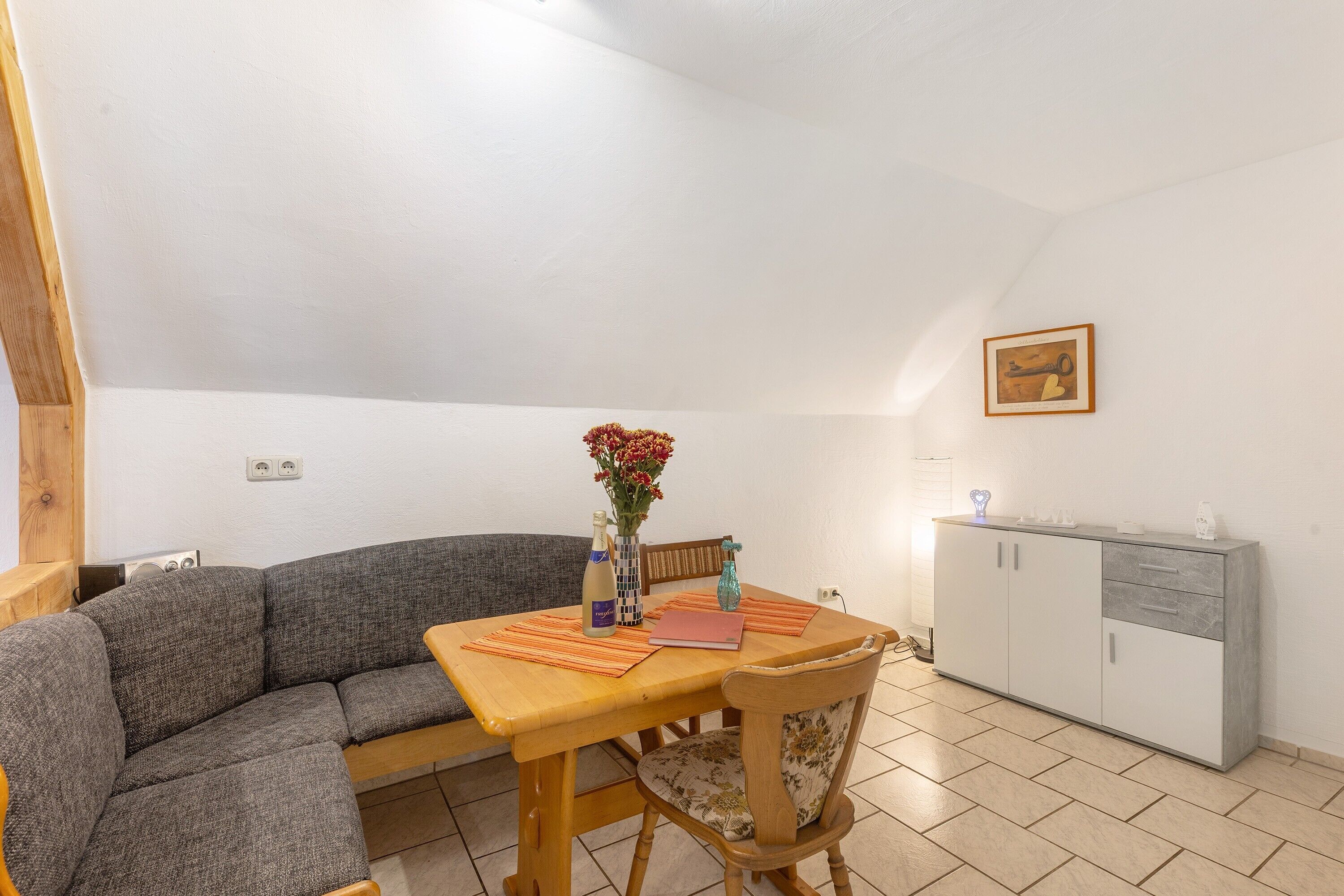 Une pièce comprenant un canapé, une table à manger, un buffet et un vase avec des fleurs.