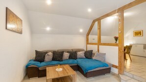 A modern interior with a sectional sofa, a wooden table, and a kitchen area visible through an open doorway. - Apartment 'Sonnenblume' with Balcony and Wi-Fi (Lichtenfels)