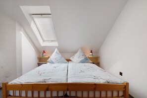 A bedroom with a sloped ceiling, a skylight, a wooden bed frame, two bedside tables with lamps, and a patterned bedspread.