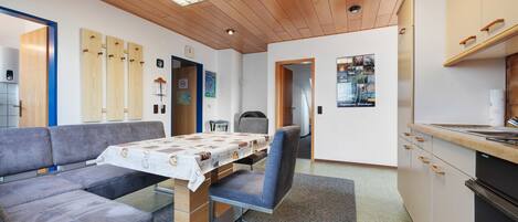 Eine moderne Küche mit Holzschränken, einem Esstisch mit Tischdecke, einem grauen Sofa und einem kleinen Kühlschrank.