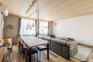 Een moderne woonkamer met een eethoek, een grijze bank en een televisie.