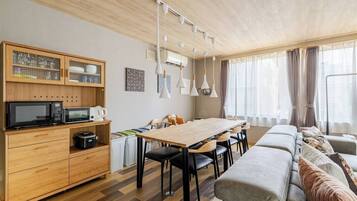 A modern living room with a wooden dining table, black chairs, a sofa, and a kitchen area with a microwave and cabinets.