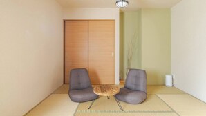 Una habitación con suelo de esteras de tatami, dos sillas grises, una mesita redonda y una puerta corredera de madera.