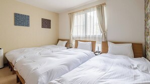 Habitación de hotel con dos camas, una mesita de noche con lámpara y una ventana con cortinas traslúcidas.