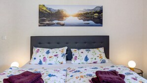 Un lit avec une literie à motifs floraux, une tête de lit et un tableau représentant un lac accroché au mur.