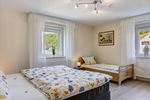 Een slaapkamer met twee bedden, een nachtkastje met een lamp, een raam met gordijnen en een schilderij aan de muur.