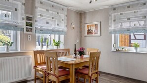 Un coin repas avec une table et des chaises en bois, une fenêtre donnant sur un paysage agréable et une horloge fixée au mur.
