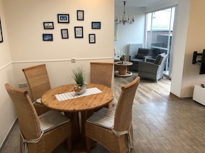 A dining area with a round wooden table, four wicker chairs, a potted plant, and framed pictures on the wall.