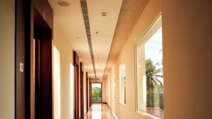 Un largo pasillo bien iluminado con piso pulido, ventanas amplias y puertas a un lado.