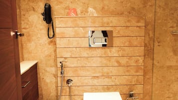 Een moderne badkamer met een marmeren wand, toilet, douche en een houten kast.