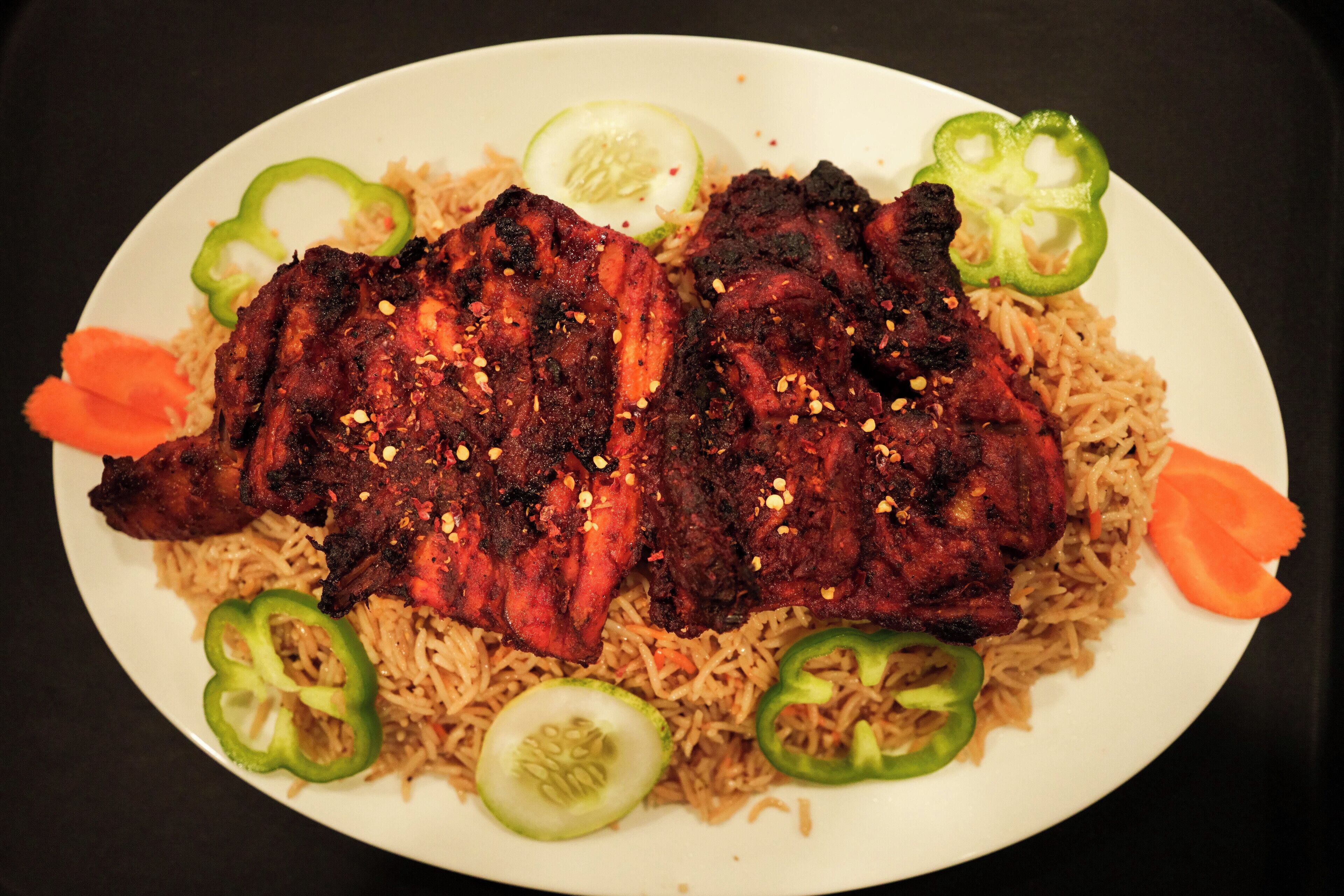 Une assiette de viande grillée et de riz, garnie de tranches de concombre et de poivron vert.