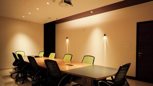 Un salón de conferencias con una larga mesa, sillas negras y dos luces fijadas a la pared.