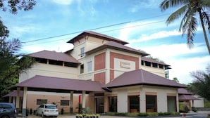 Un hotel de dos plantas con tejado rojo y paredes color beige, que cuenta con un área de estacionamiento techada y un letrero que dice "ValuVand Resort".