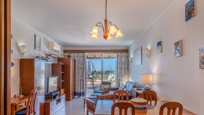 A spacious living area with a dining table, chairs, a sofa, and a TV. There is a balcony with a view of the sea. - Sol Beach View Terrace by Interhome (Ferragudo)