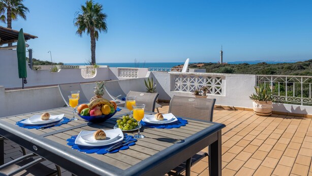 A table set for breakfast with a view of the sea, palm trees, and a lighthouse in the background. - Sol Beach View Terrace by Interhome (Ferragudo)