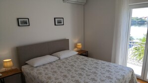 Een slaapkamer met een bed, twee nachtkastjes met lampen, een raam met uitzicht op een wateroppervlak en twee ingelijste foto’s aan de muur.