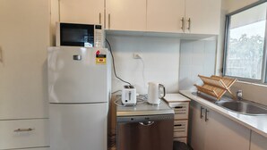 A compact kitchen with a white refrigerator, a microwave, a toaster, and a dishwasher. There is a window providing natural light and a view of greenery outside. - 15 mins to Airport|Gateway to NSW (Campbellfield)