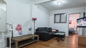 A modern living room with a black sofa, a wooden coffee table, and a TV mounted on the wall. - 15 mins to Airport|Gateway to NSW (Campbellfield)