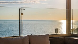 Une pièce avec vue sur la mer, une balustrade en verre et un banc agrémenté de coussins.