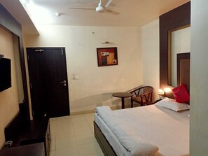 A hotel room with a bed, a chair, a desk, a TV, and a door.
